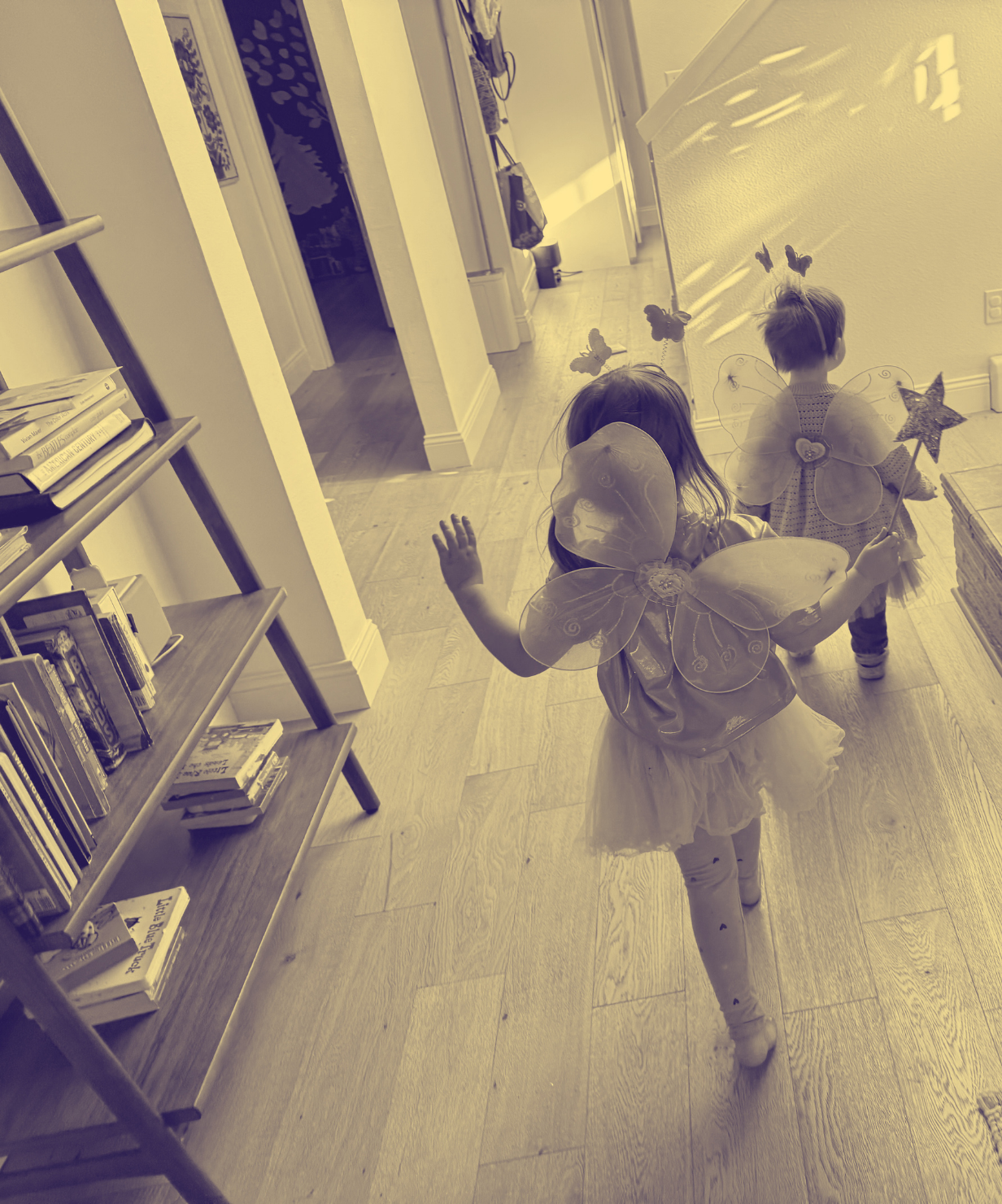 Two children in fairy wings walking down a sunlit hallway